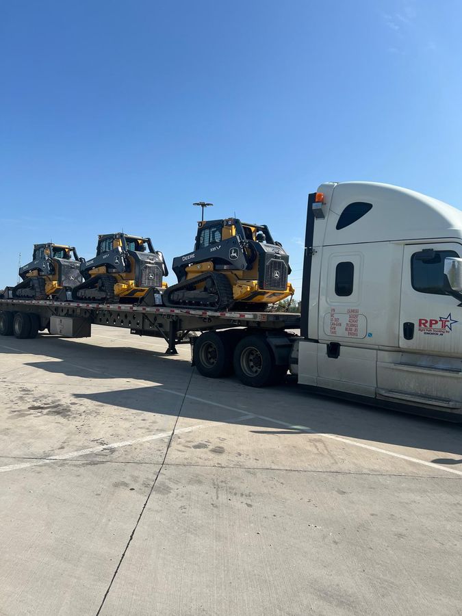 Skid-steer loaders loaded and secured on a Right Path Trucking flatbed trailer